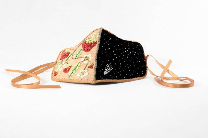 Mask made with birch bark. One half on a tan background has strawberries, green leaves and white flowers. The other half is black with a comet and small beads.